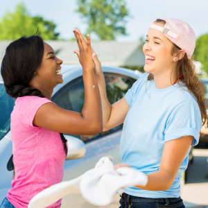 two young girls high fiving each other at a car wash raising funds to give to charity