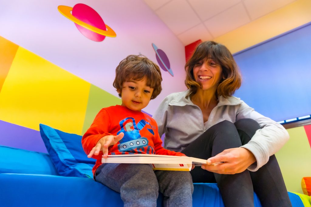 Woman teacher playing with a child reading a book and having fun, Interior of a kindergarten